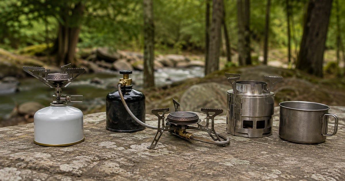 Several types of camping stoves side by side outdoors with a cook pot