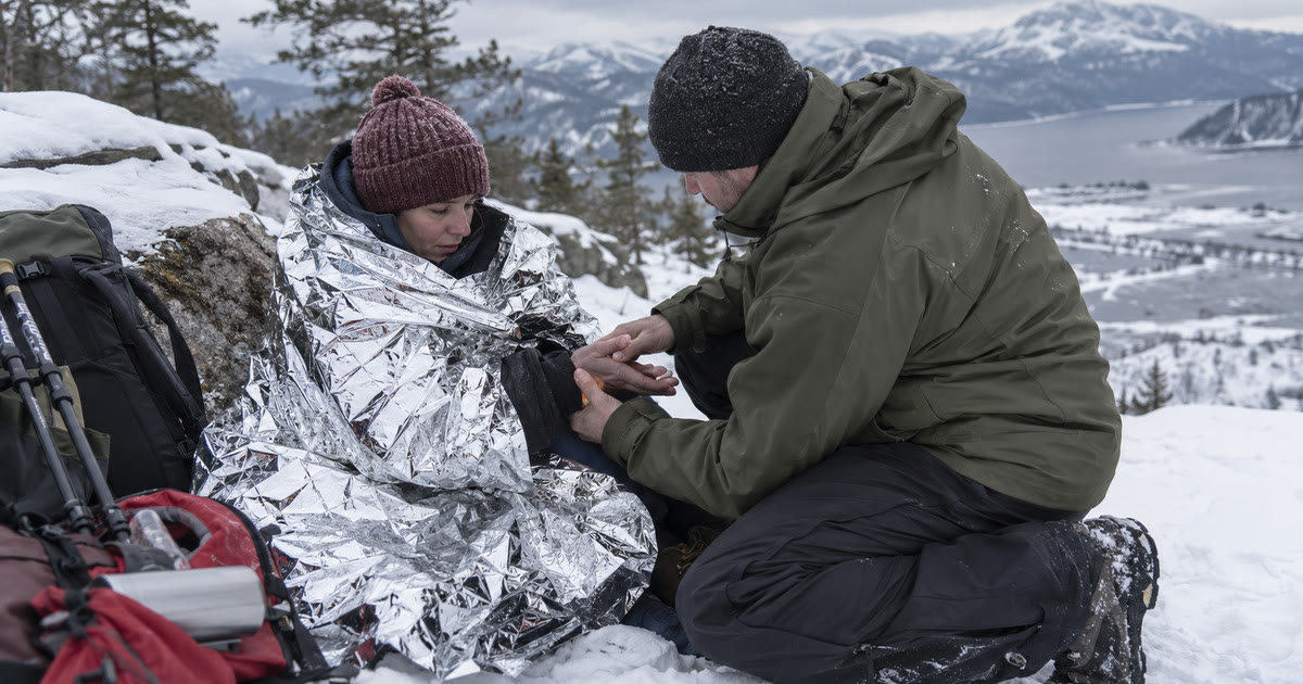 Wrapping a cold, wet person in an emergency thermal blanket outdoors in the snow
